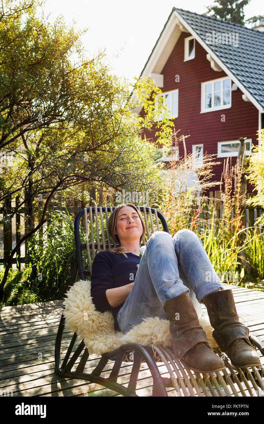 Mitte Erwachsene Frau entspannend auf Liegestuhl auf Holzterrassen Stockfoto