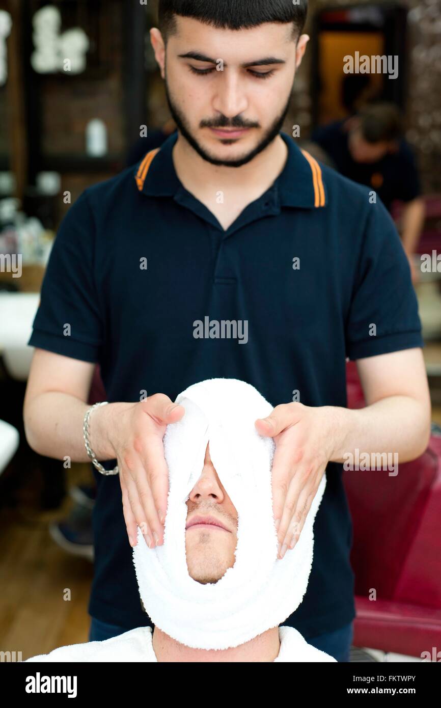 Barber Umhüllung junge mans Gesicht in frisches Handtuch, Blick nach unten Stockfoto