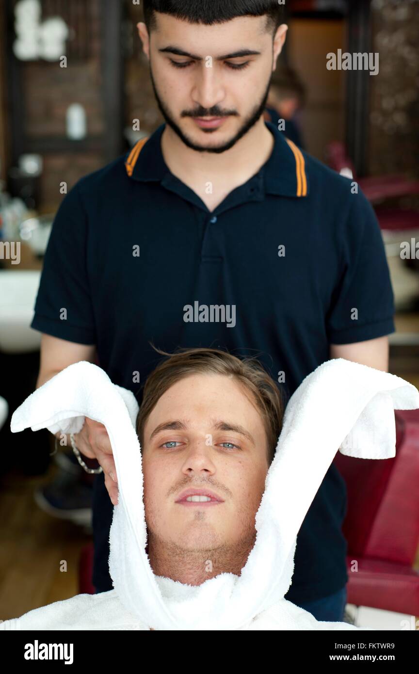 Barber Umhüllung junge mans Gesicht in frisches Handtuch, Blick nach unten Stockfoto