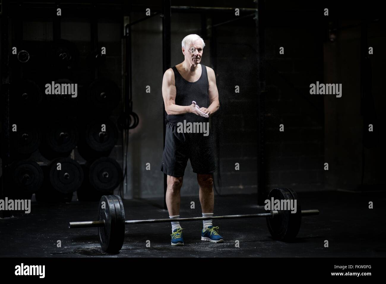 Senior woman Kreidung Hände für Gewichtheben in dunklen Turnhalle Stockfoto