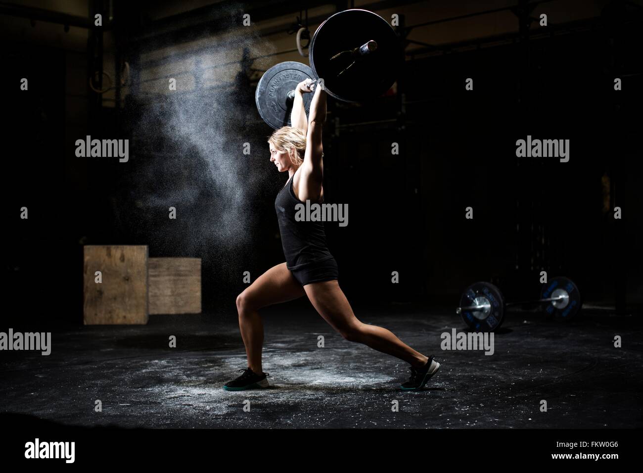 Seitenansicht der jungen Frau Gewichtheben Langhantel in dunklen Turnhalle Stockfoto