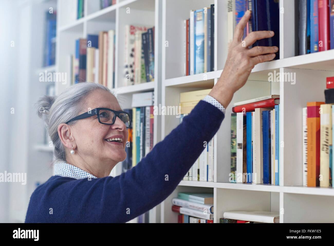 Glücklich grau behaarte Reife Frau Bücherregale Buch auswählen Stockfoto