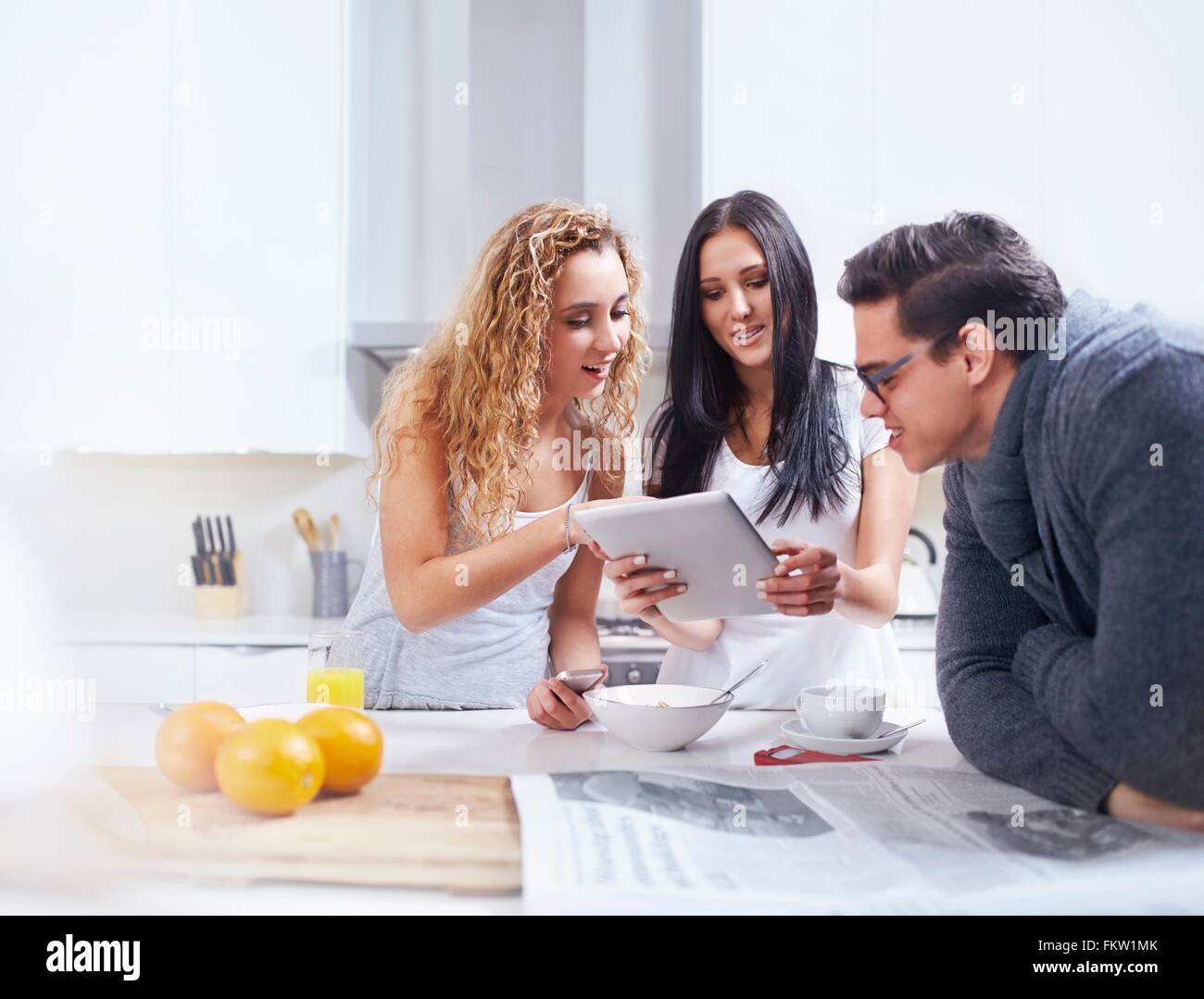 Drei junge Erwachsene, die mit digital-Tablette am Küchentisch Stockfoto