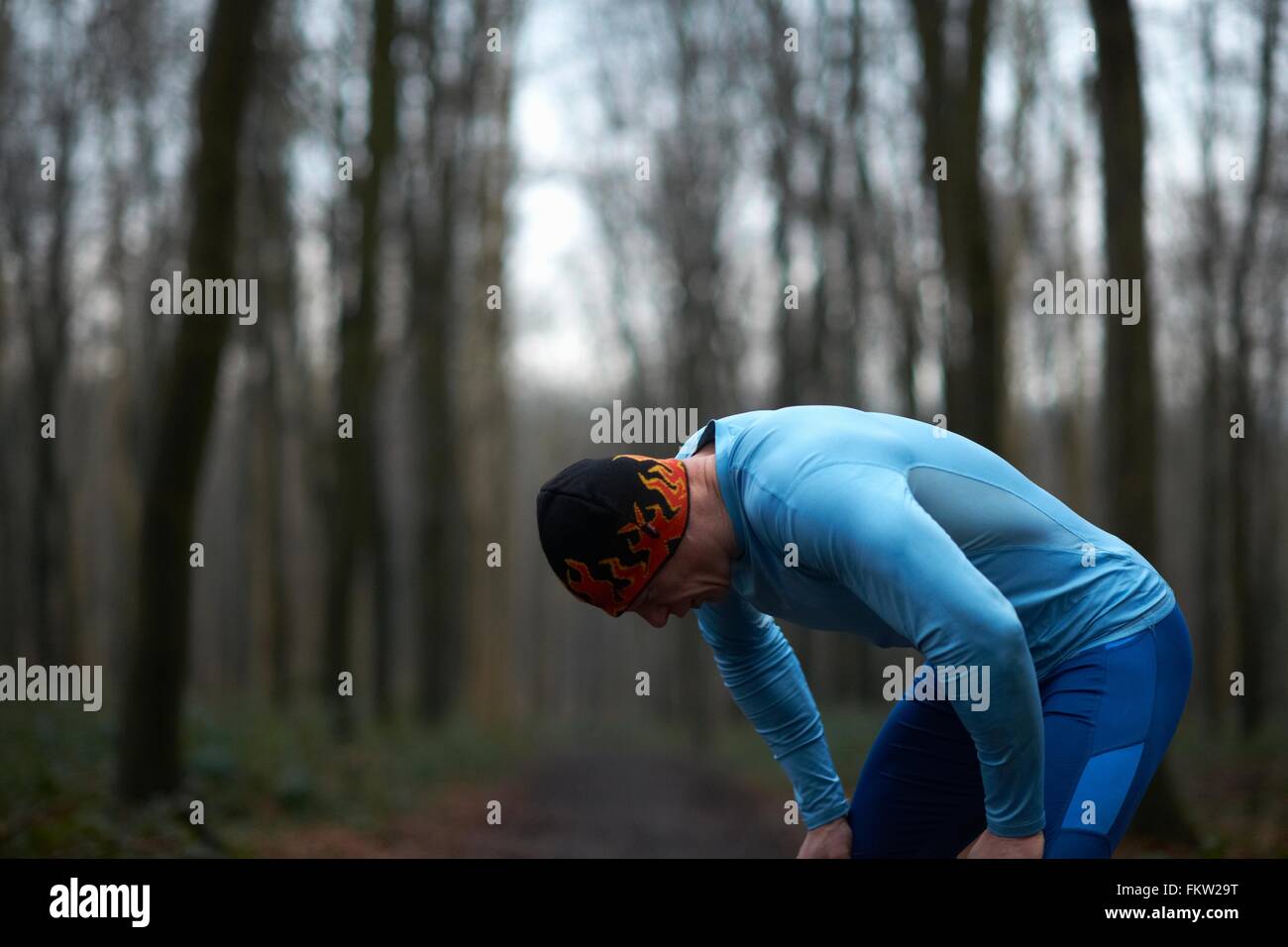 Läufer mit Stricken Hut und Elasthan Biegung nach vorne Hände auf Knien erschöpft Stockfoto