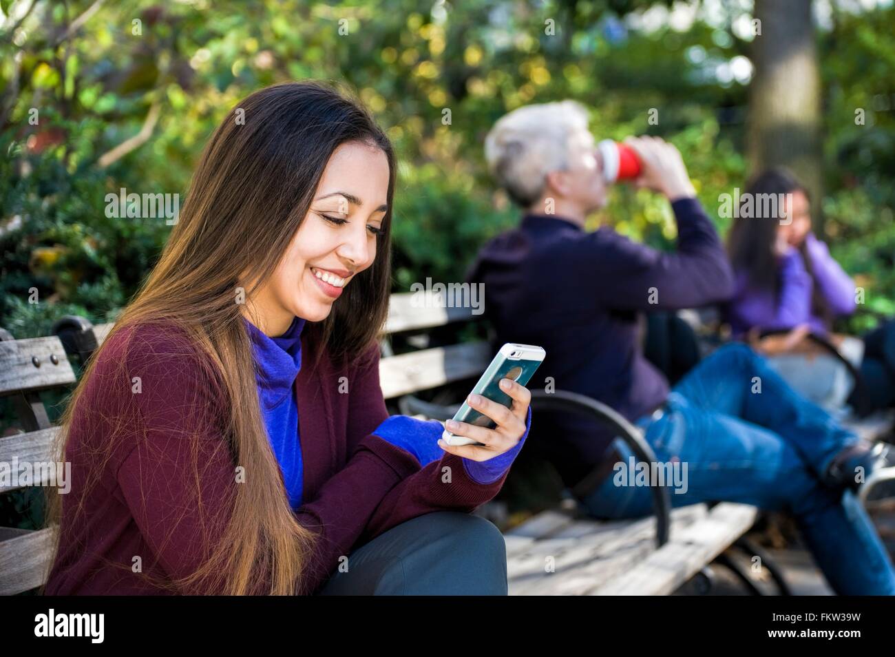 Junge Frau sitzt auf der Parkbank Smartphone Texte lesen Stockfoto