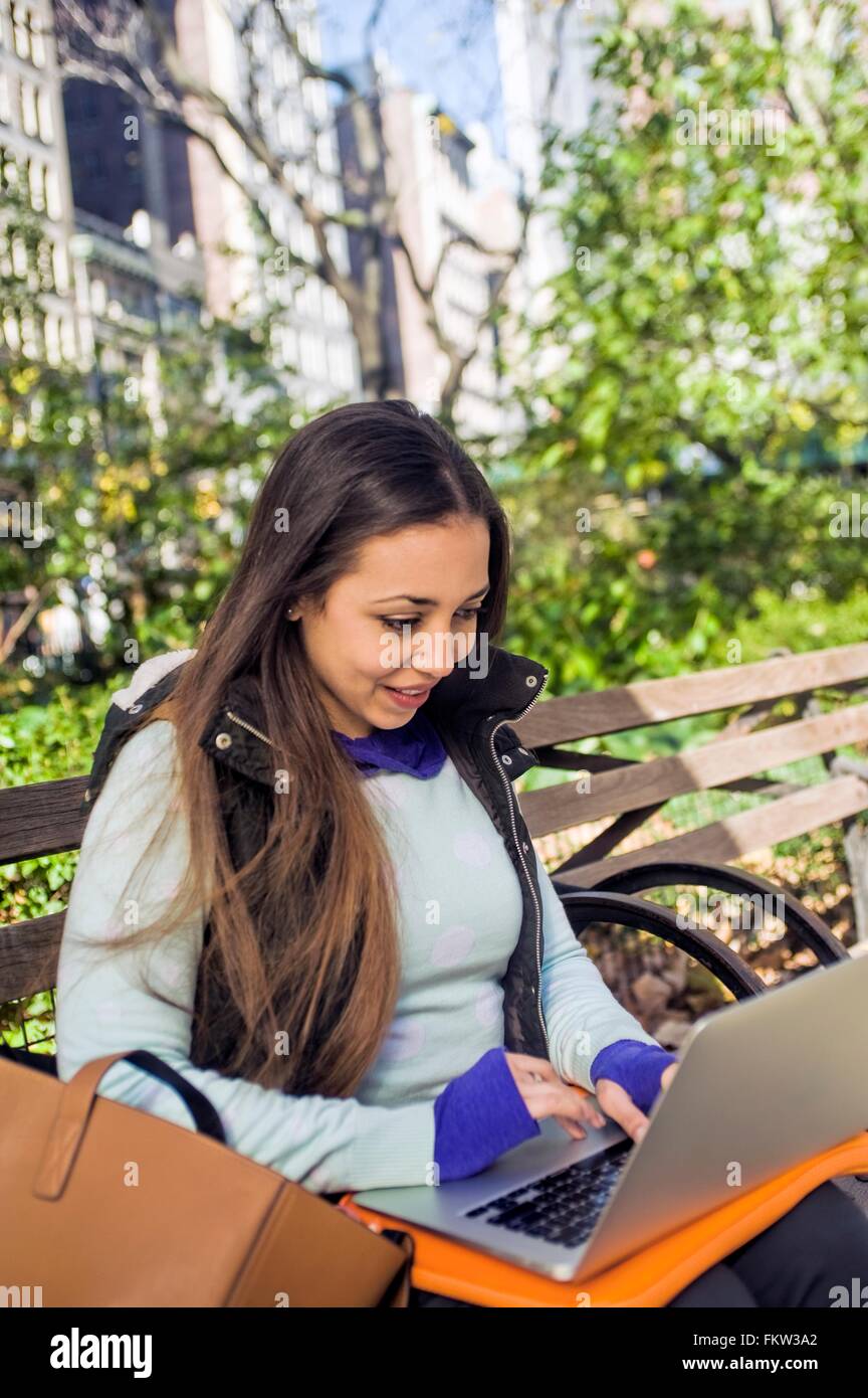 Junge Frau sitzt auf der Parkbank Tippen auf laptop Stockfoto