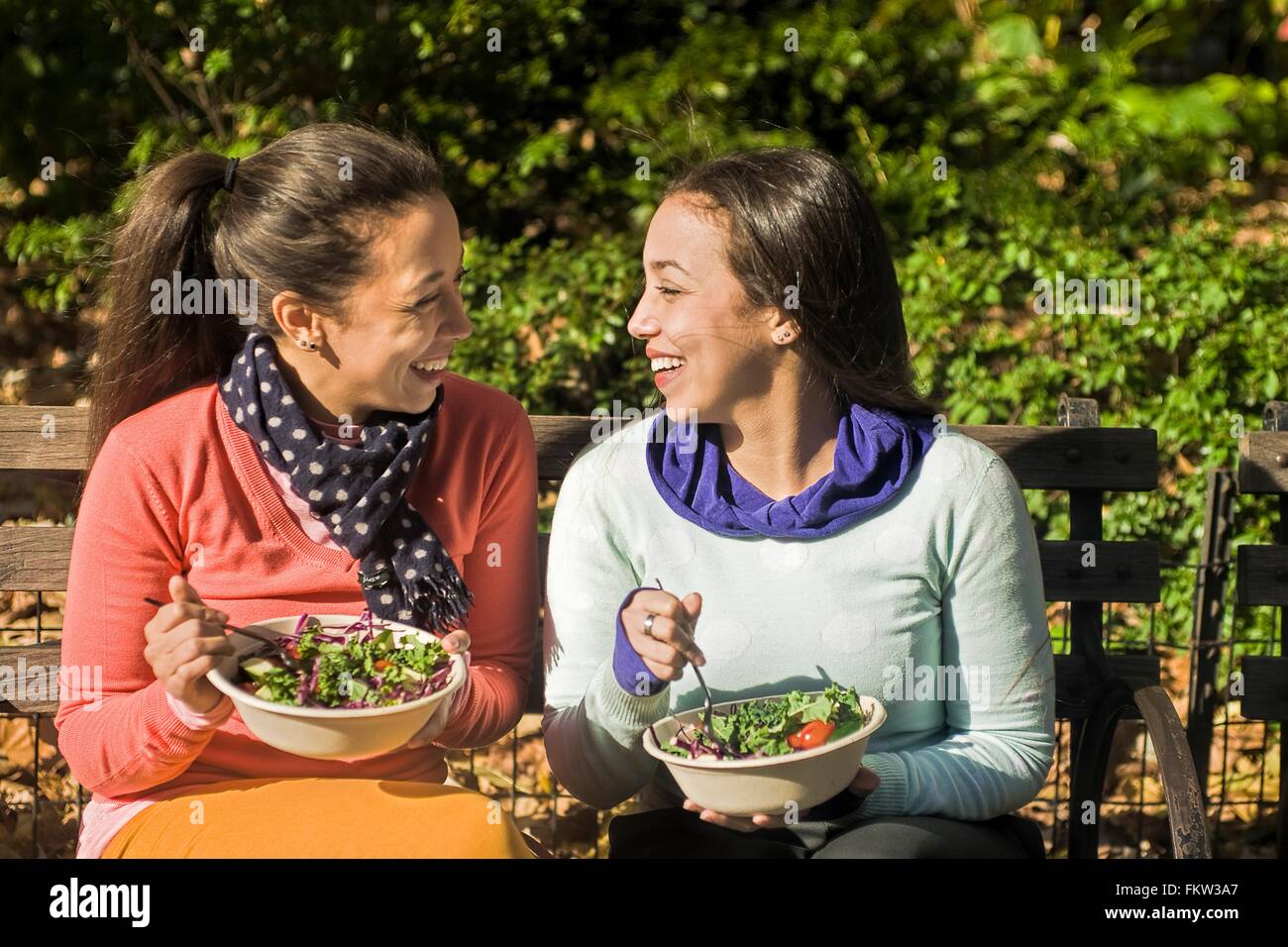 Junge Erwachsene weibliche Zwillinge auf Parkbank beim Mittagessen sitzen Stockfoto
