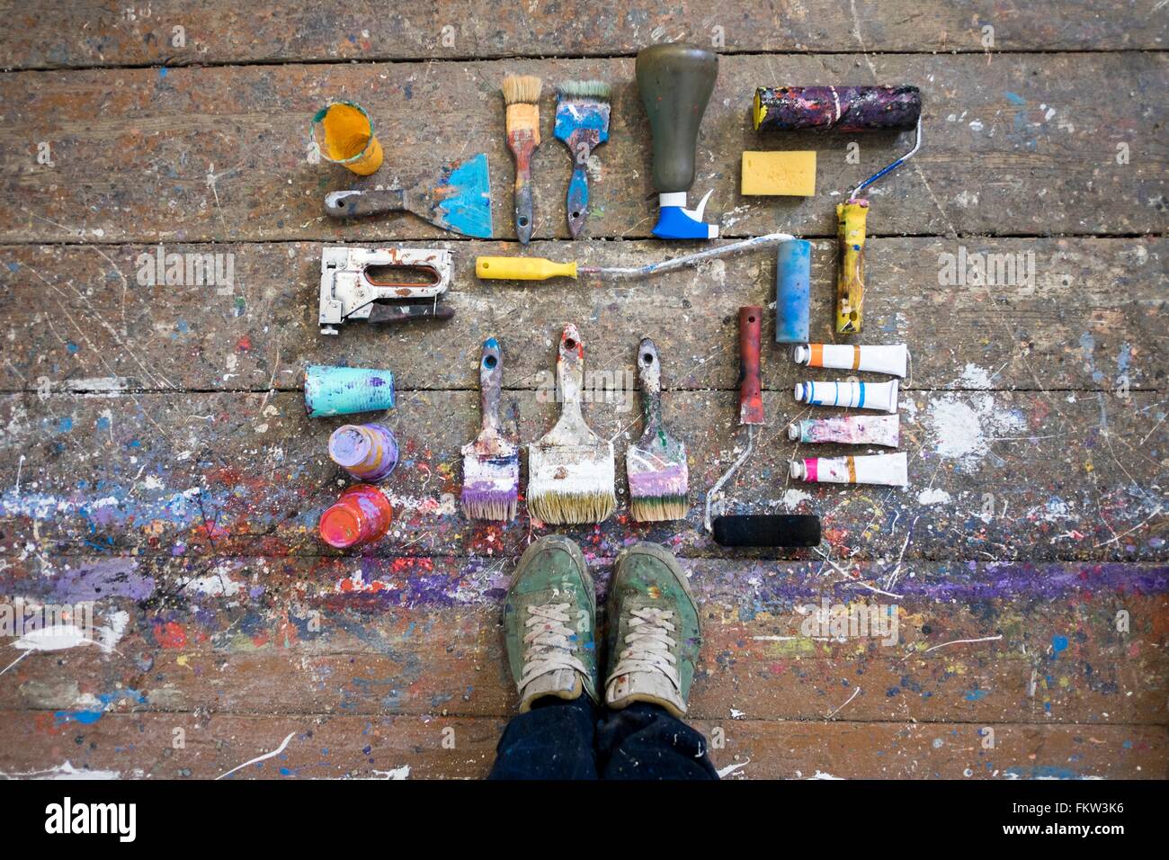Draufsicht der Künstler Füße und Kunst Ausrüstung auf Lack bespritzt Diele Stockfoto