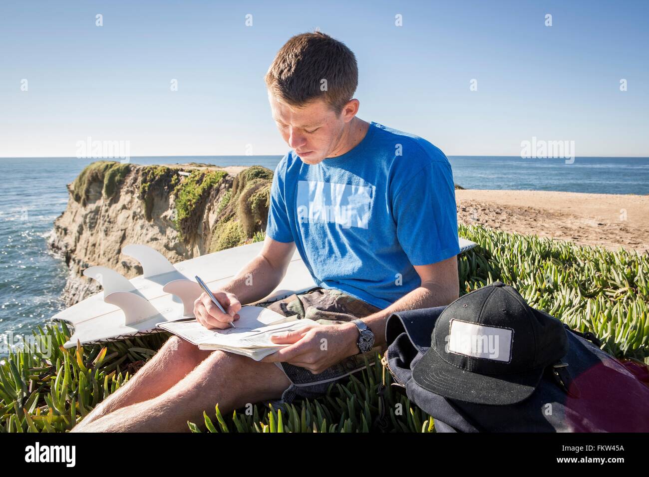Junger Mann sitzen Klippe, in Buch schreiben Stockfoto