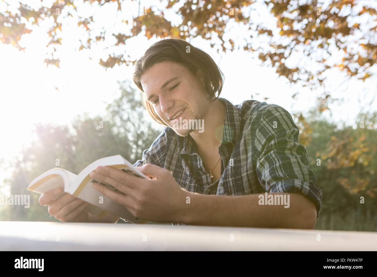 Junger Mann im Freien sitzen am Tisch, Buch, blickte lächelnd Stockfoto