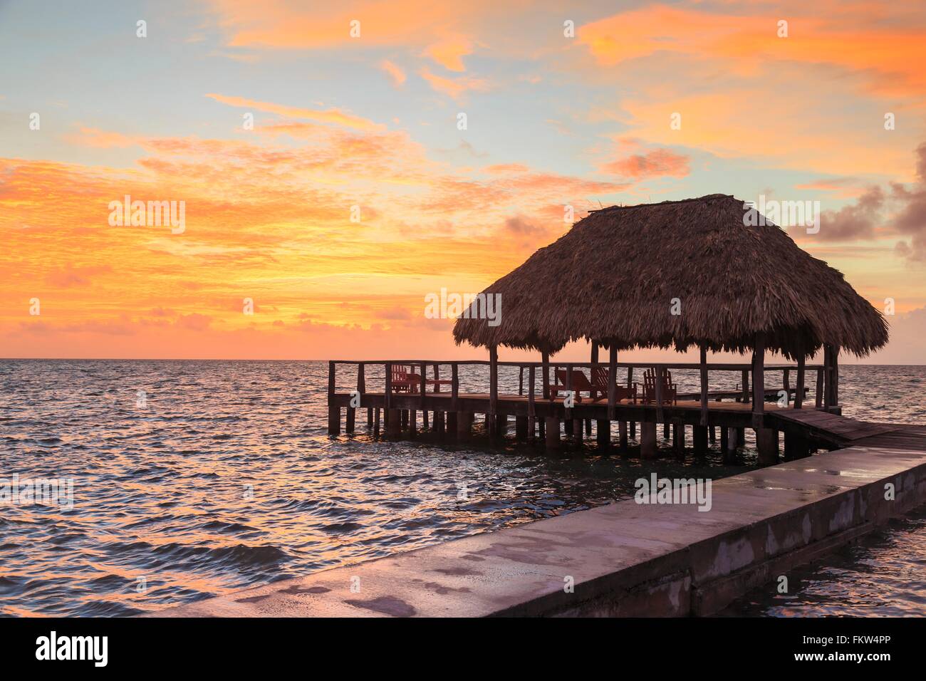 Gestelzt Waterfront Pier und Strohdach bei Sonnenuntergang, St. Georges Caye, Belize, Mittelamerika Stockfoto