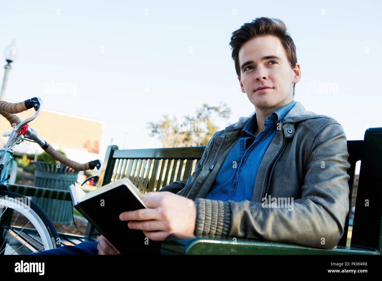 Junger Mann Lesebuch auf Parkbank Stockfoto