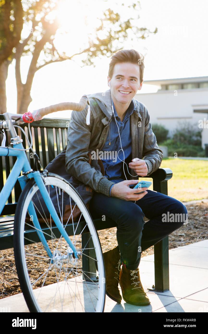 Junger Mann Kopfhörer Musik hören auf sonnigen Parkbank Stockfoto