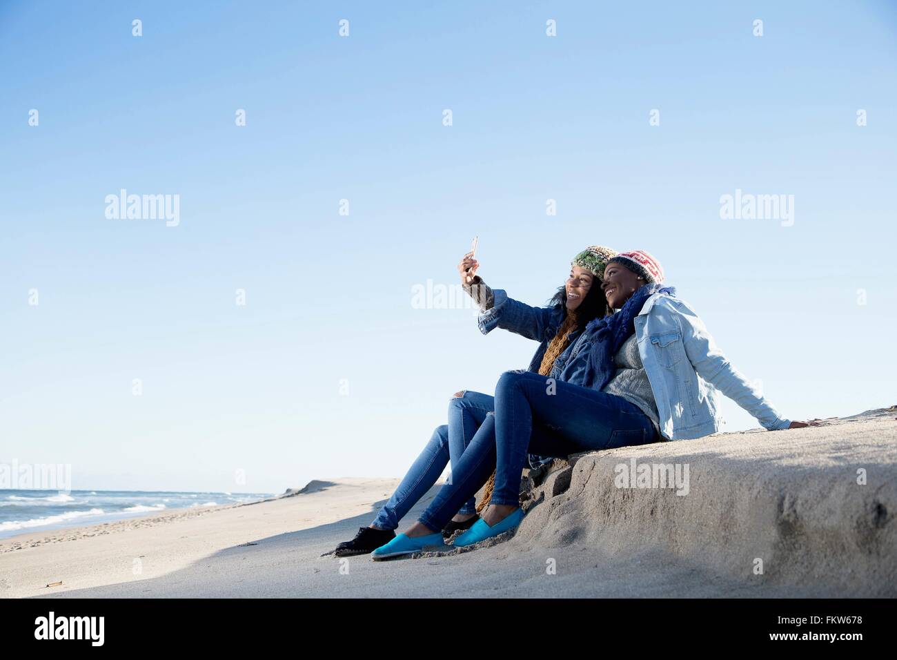 Zwei Freunde sitzen am Strand, wobei Selbstbildnis, mit smartphone Stockfoto