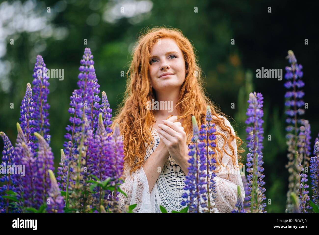 Ruhige junge Frau unter lila Wildblumen mit den Händen umklammert Stockfoto