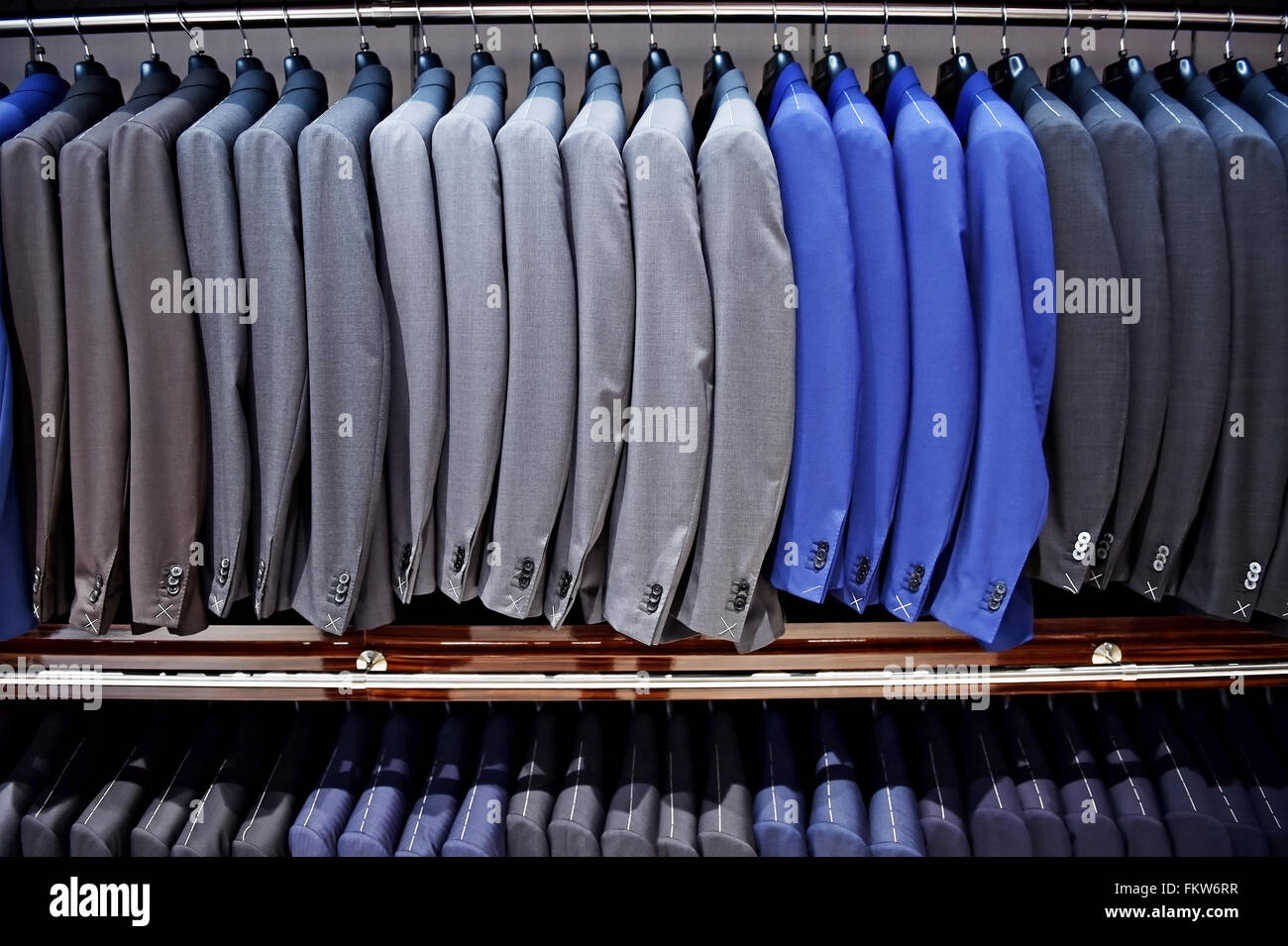 Elegante blaue und graue Anzüge auf Kleiderbügeln werden in einem Anzug-Shop gesehen. Stockfoto