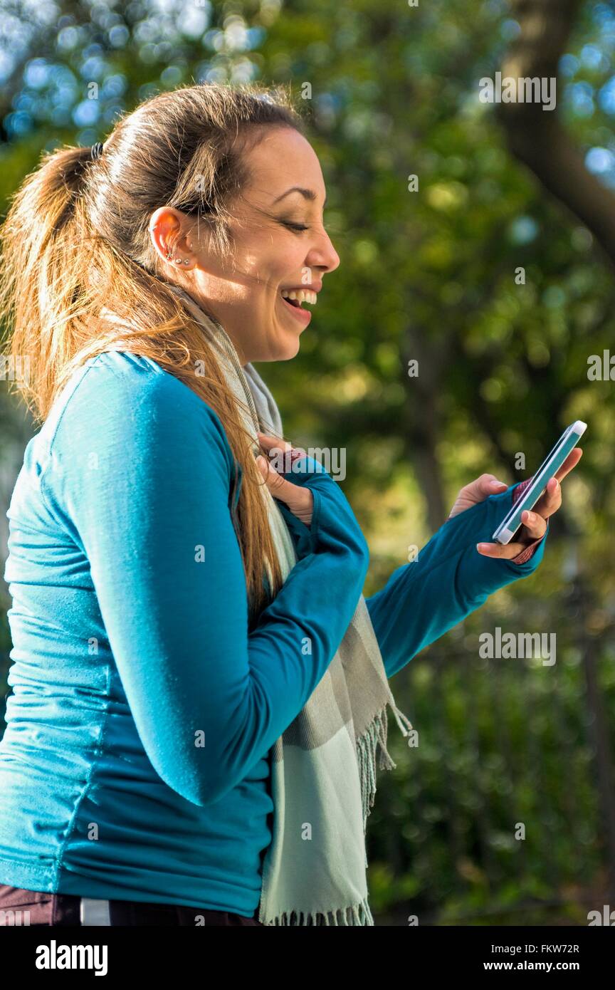 Junge Frau lächelte Nachricht auf Smartphone im park Stockfoto