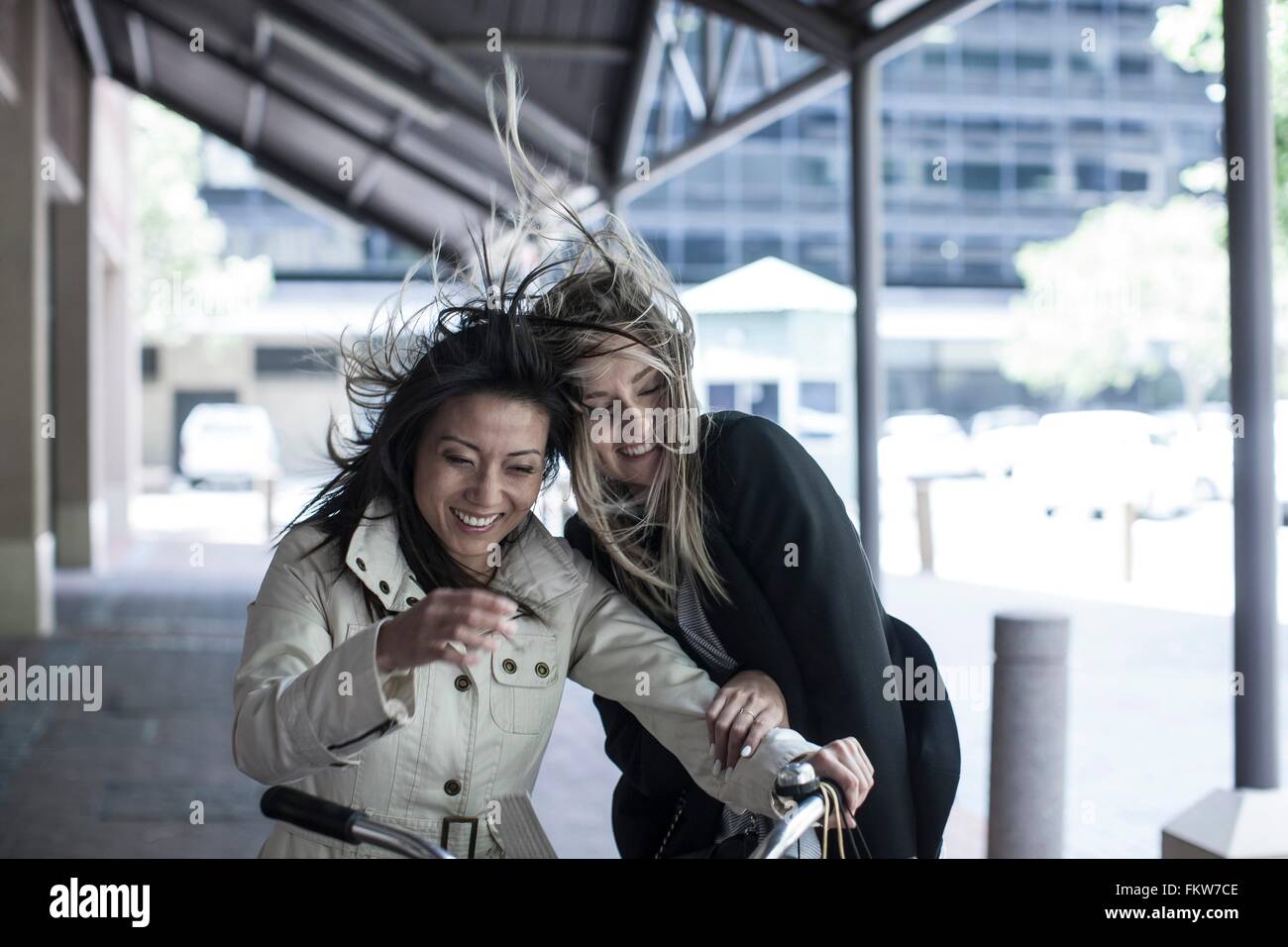 Zwei Freundinnen mit Überseerennen Haar lachend auf dem Fahrrad in die Stadt Stockfoto