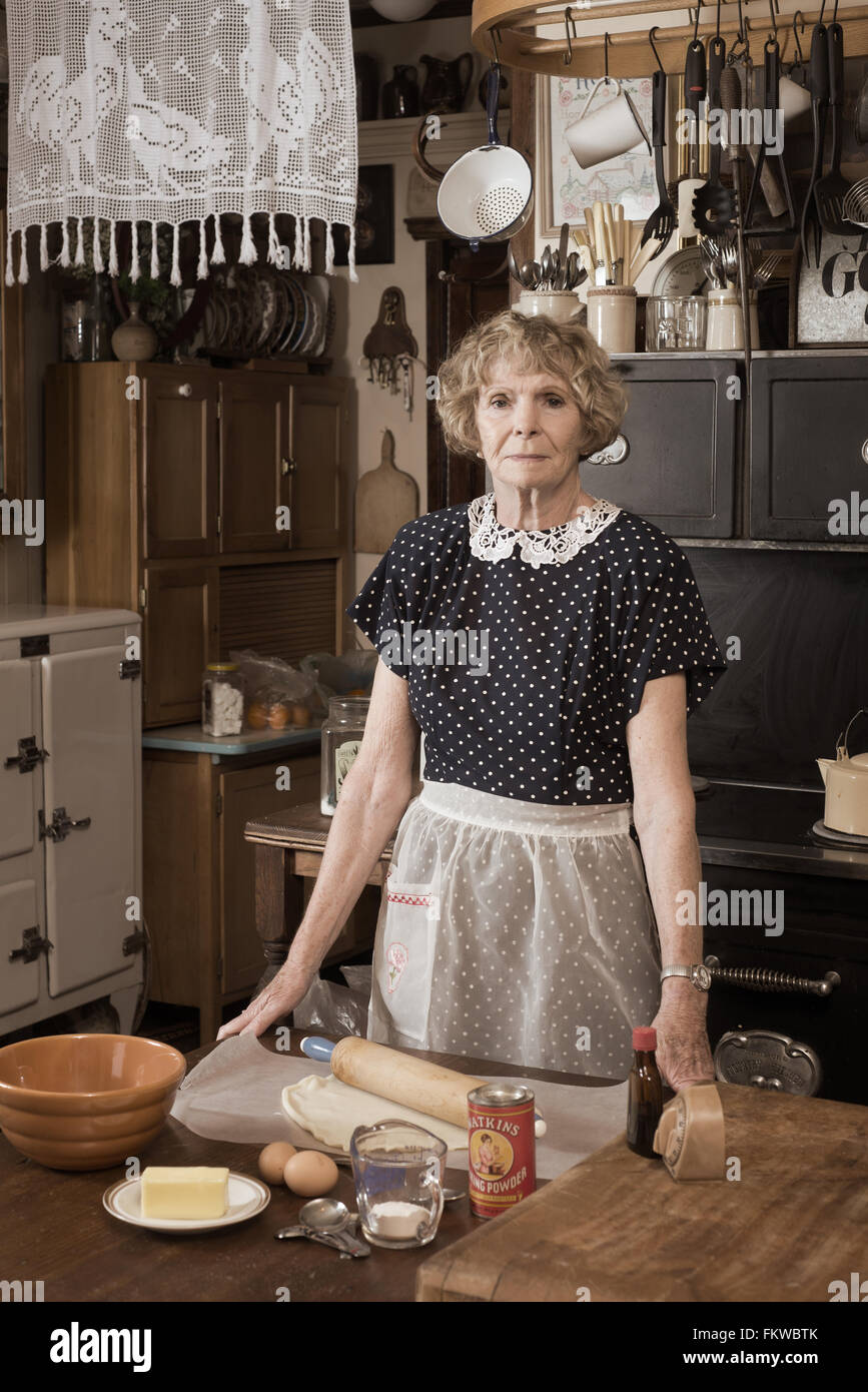 Ein Retro-Stil Foto einer Frau in 1940 Stil Kleid und Küche umgeben von antiken Artefakte mit Zutaten zum Backen ein p Stockfoto