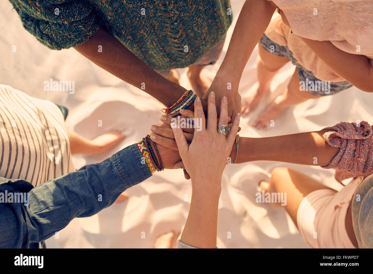 Gruppe von jungen Männern und Frauen zeigen Einheit. Gruppe junger Freunde setzen ihre Hände zusammen am Strand. Stockfoto
