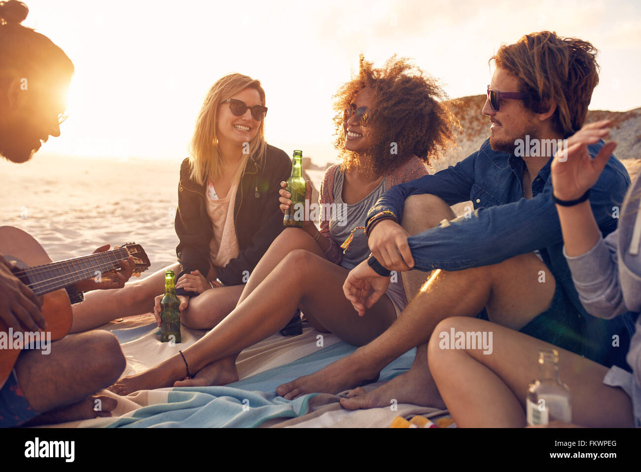 Porträt der Gruppe junger Freunde mit einer Party am Strand abends. Männer und Frauen trinken Bier und Freund anhören Stockfoto