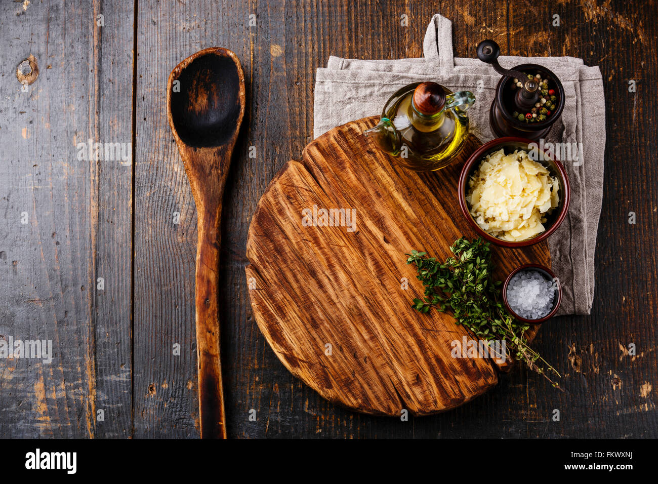 Schneidebrett, alten Holzlöffel, Gewürzen und Parmesan-Käse auf dunklem Holz Stockfoto