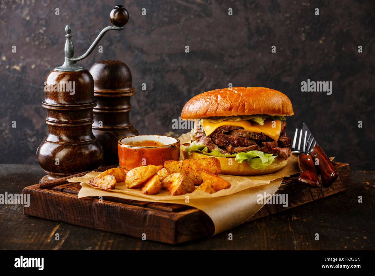 Pastrami-Burger mit in Scheiben geschnittenen Braten Rindfleisch und Kartoffel Wedges auf dunklem Hintergrund Stockfoto