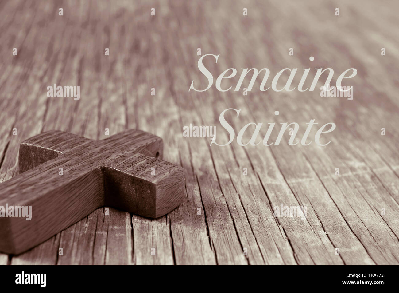 Nahaufnahme von einem kleinen Holzkreuz auf einer rustikalen Holzoberfläche und der Text Semaine Sainte, Karwoche in Französisch, in Sepia Tönung Stockfoto