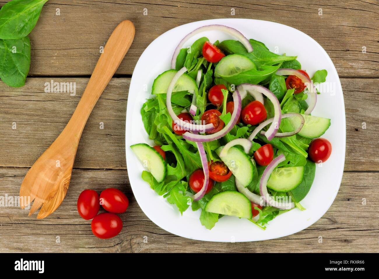 Salat mit Gemüse, Cherry-Tomaten, rote Zwiebeln und Gurken auf weißen Teller mit Holz Hintergrund, Draufsicht mit Gabel Stockfoto