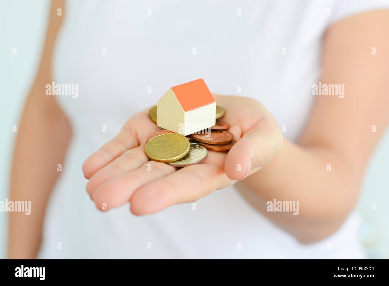 Frau Hand hält Haus und Geld, was auf die steigende Kosten der Immobilienpreise Stockfoto