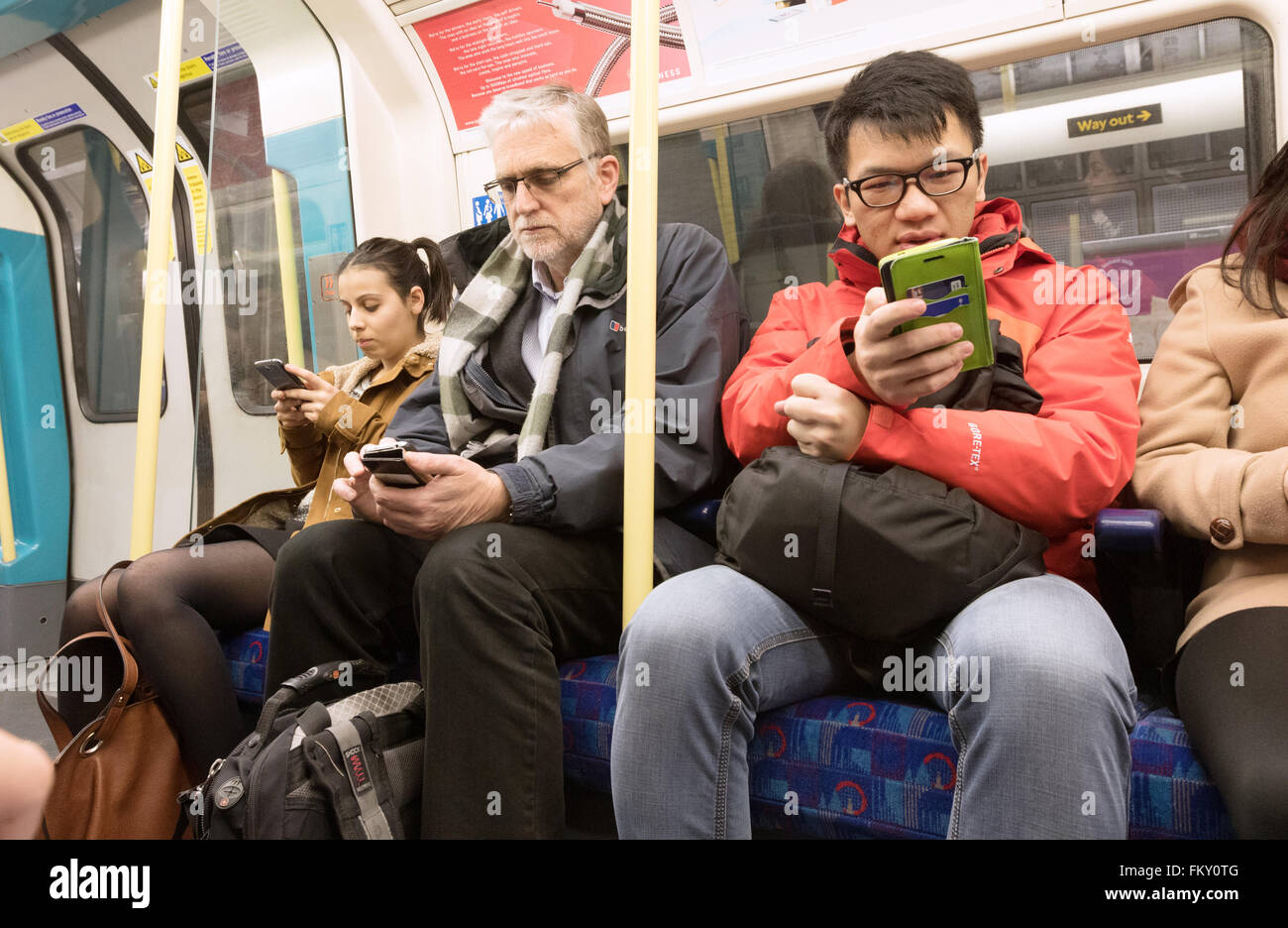 Mobiltelefone im öffentlichen Verkehr; Passagiere, die Mobiltelefone in einer Eisenbahn-Kutsche der Londoner U-Bahn, London UK, verwenden Stockfoto