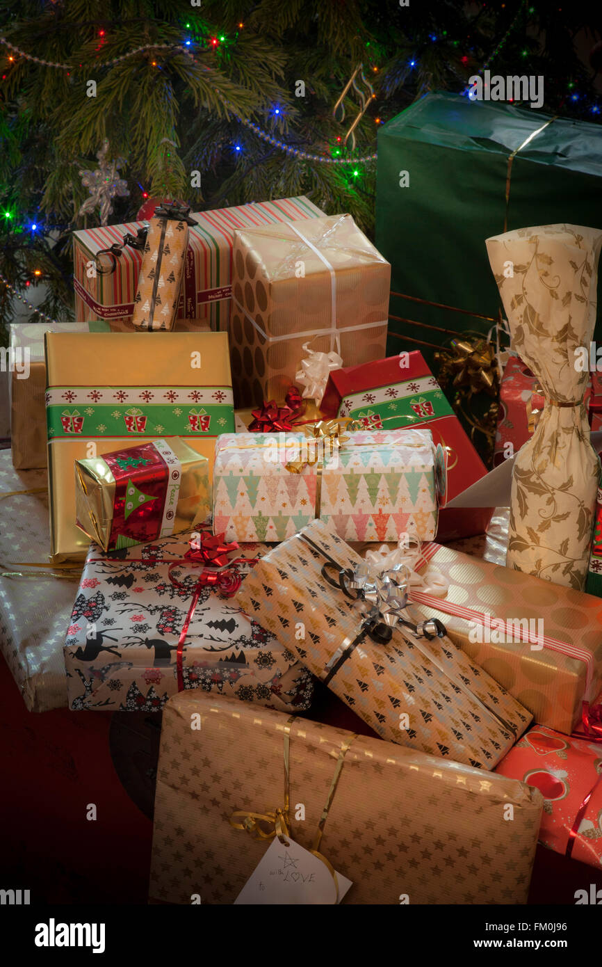 Ein Haufen elegant verpackte Weihnachtsgeschenke. Teil eines Weihnachtsbaumes mit Lichtern bildet den Hintergrund. Stockfoto
