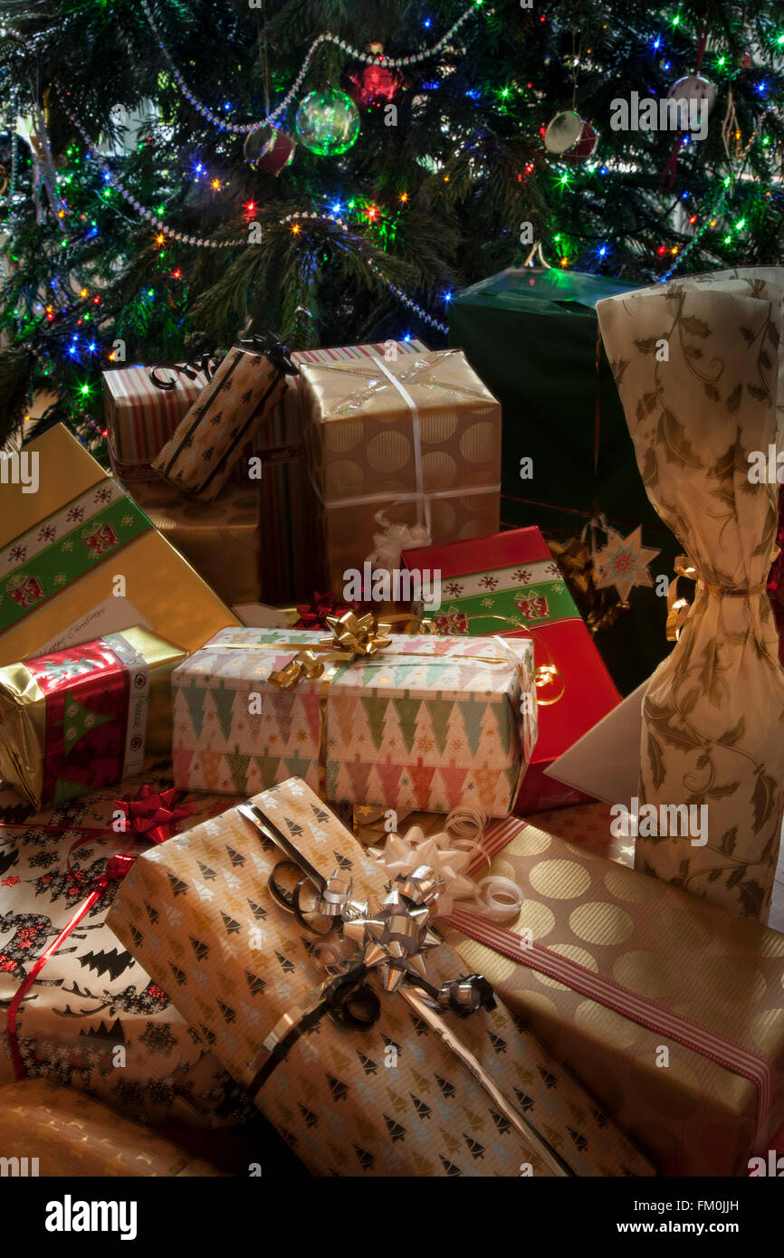 Ein Haufen elegant verpackte Weihnachtsgeschenke. Teil eines Weihnachtsbaumes mit Lichtern bildet den Hintergrund. Stockfoto