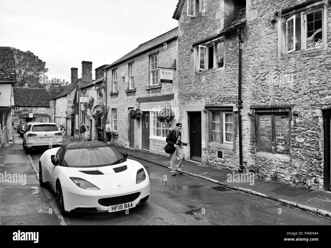 Lotus Auto im Regen im malerischen englischen Dorf von Avebury und alten Hütten mit älteren Fotografen Touristen vorbeigehen Stockfoto