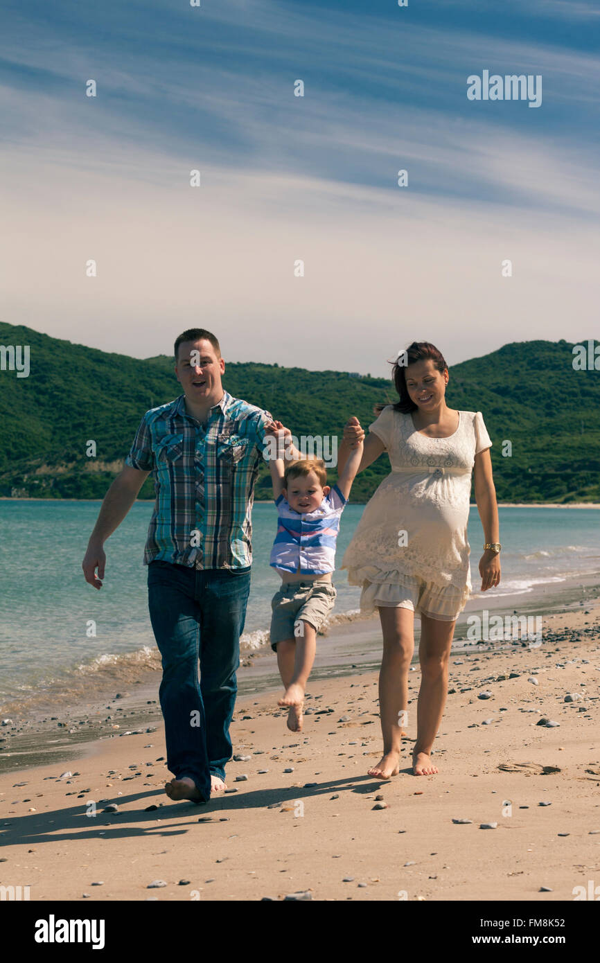 Glücklich schwanger paar und ihr Sohn sonnigen Tag zu genießen, zu springen und zu Fuß an der Küste in Spanien. Stockfoto