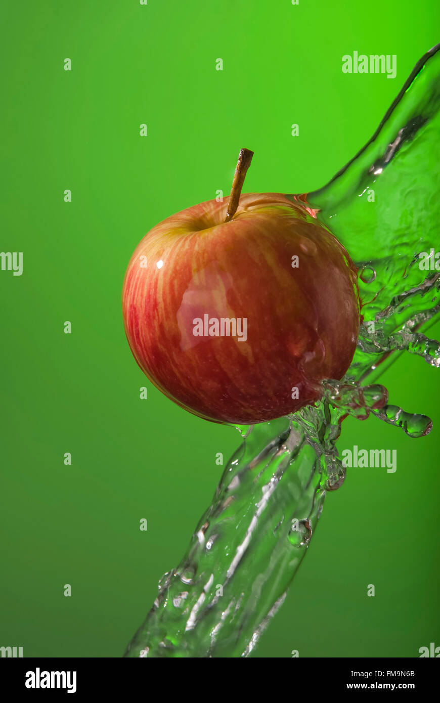 Köstliche Bio roter Apfel auf grünem Hintergrund mit Wasser Spritzen Bewegung. Ideal für gesunde Ernährung-Kampagne oder Poster. Stockfoto