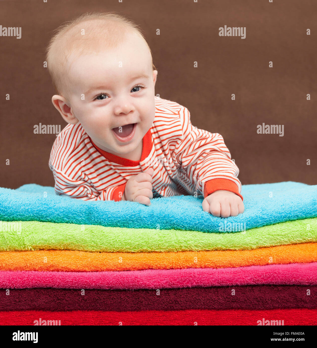 Lachendes Baby liegend auf einem Stapel von bunten Tüchern Stockfoto