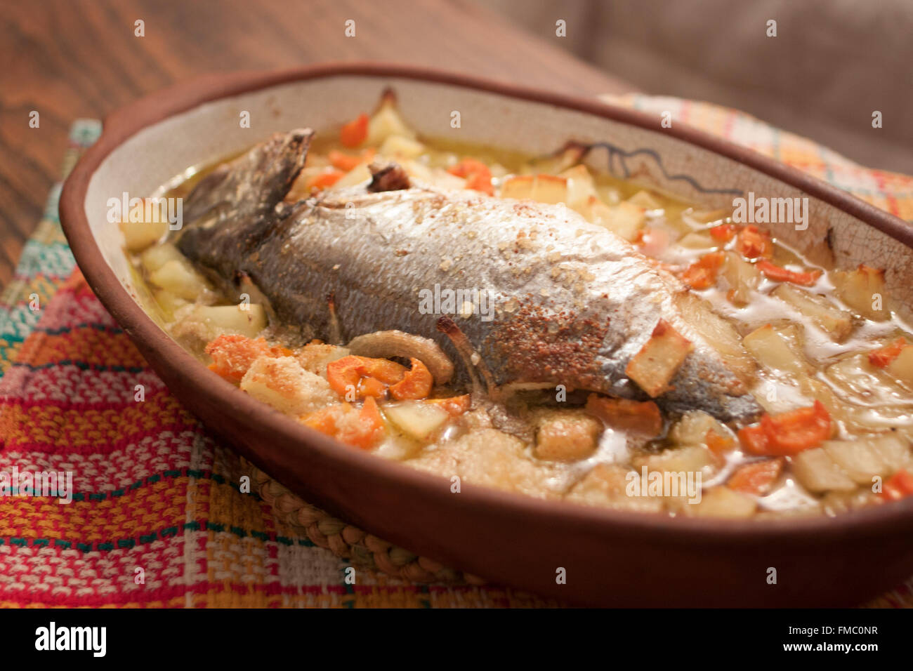 Gebackener Fisch mit Kartoffeln, Zwiebeln und Karotten auf einem Ton-Teller Stockfoto