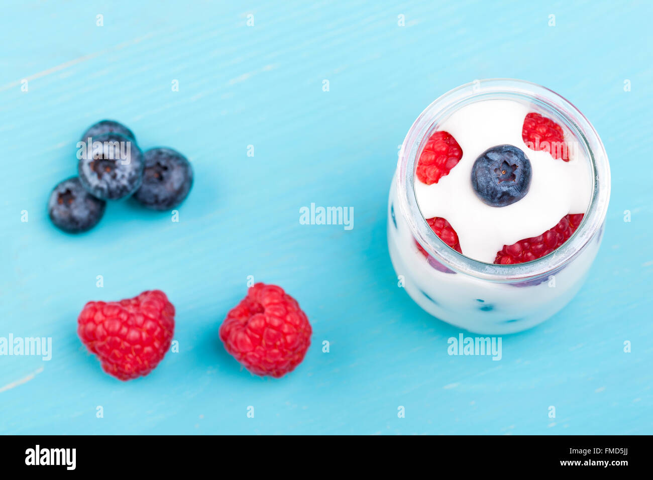 Glas Joghurt mit Beeren und Blaubeeren auf einem türkisfarbenen Holztisch Stockfoto