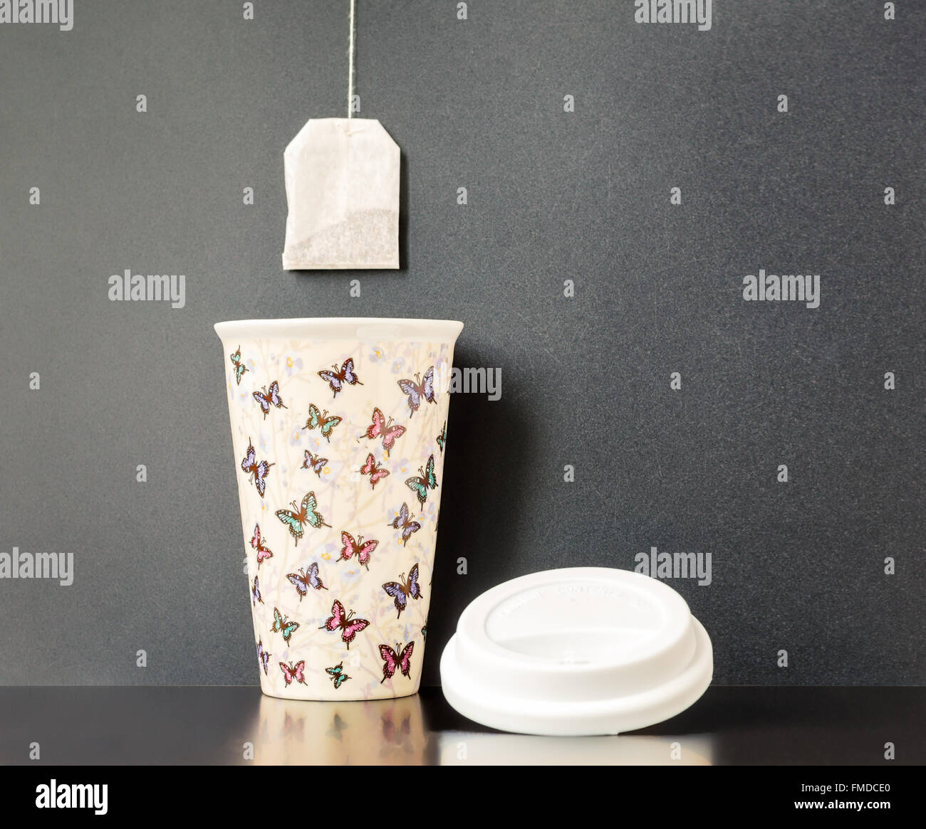 Keramik isoliert Tasse mit bunten Schmetterling Muster mit dunkelgrauen Hintergrund und einen Teebeutel drüber hängen. Stockfoto