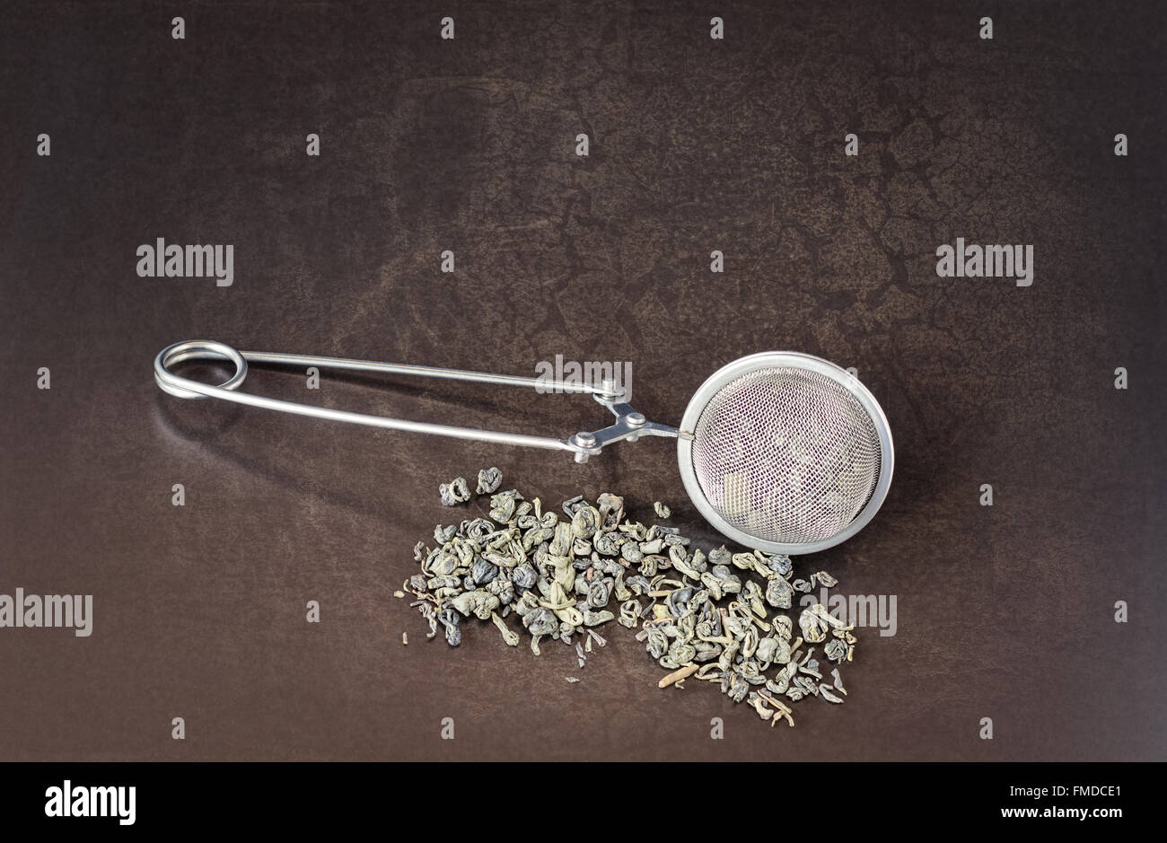 Edelstahl-Tee-Brüheinheit und Gunpowder Tee auf einem Vintage, strukturierten Hintergrund. Stockfoto