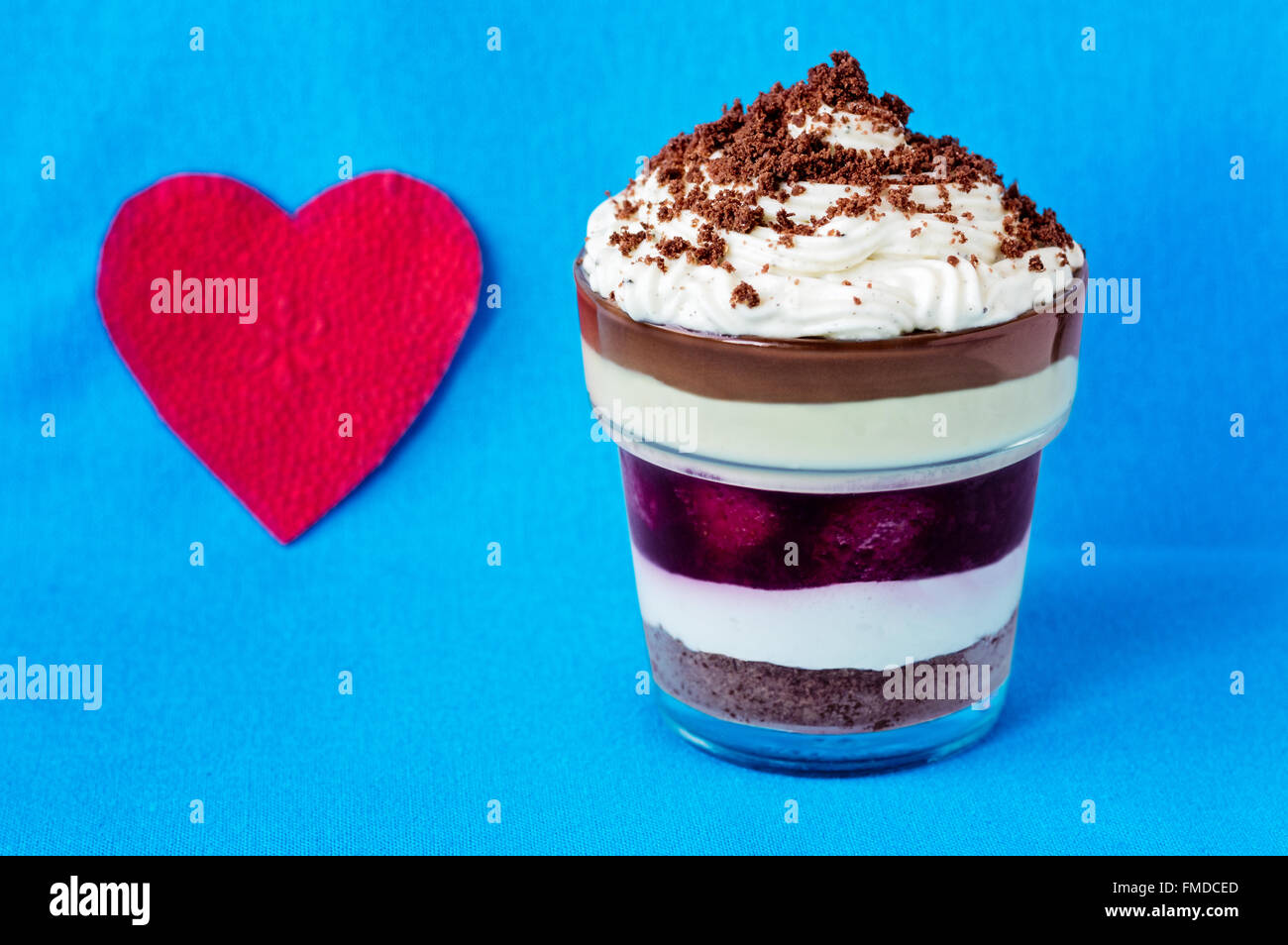 Romantische geschichtete Dessert mit zerbröselten Cookies an der Spitze in der Nähe ein Herz geformt rote Serviette auf einem hellblauen Hintergrund. Stockfoto