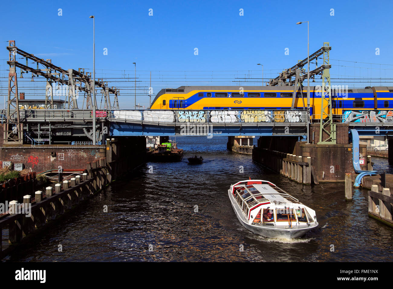 Grachtenfahrt Boot unter einer Eisenbahnbrücke mit dem Zug nach Amsterdam Centraal, Niederlande Stockfoto