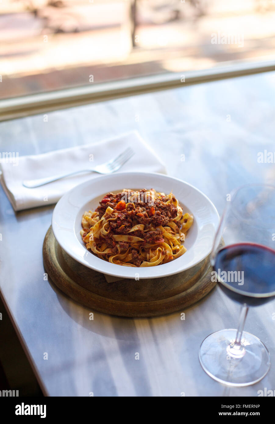 Einen Teller Spaghetti und einem Glas Rotwein für einen auf einem Tisch am Fenster sitzen. Stockfoto