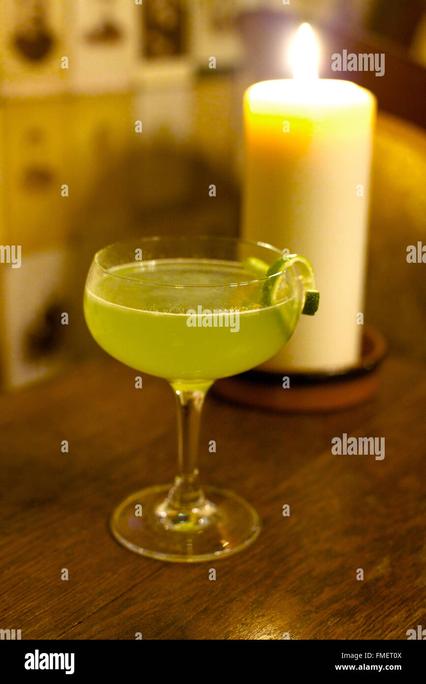 Ein grüner Cocktail sitzt auf einem hölzernen bar oben mit einer Kerze im Hintergrund. Stockfoto