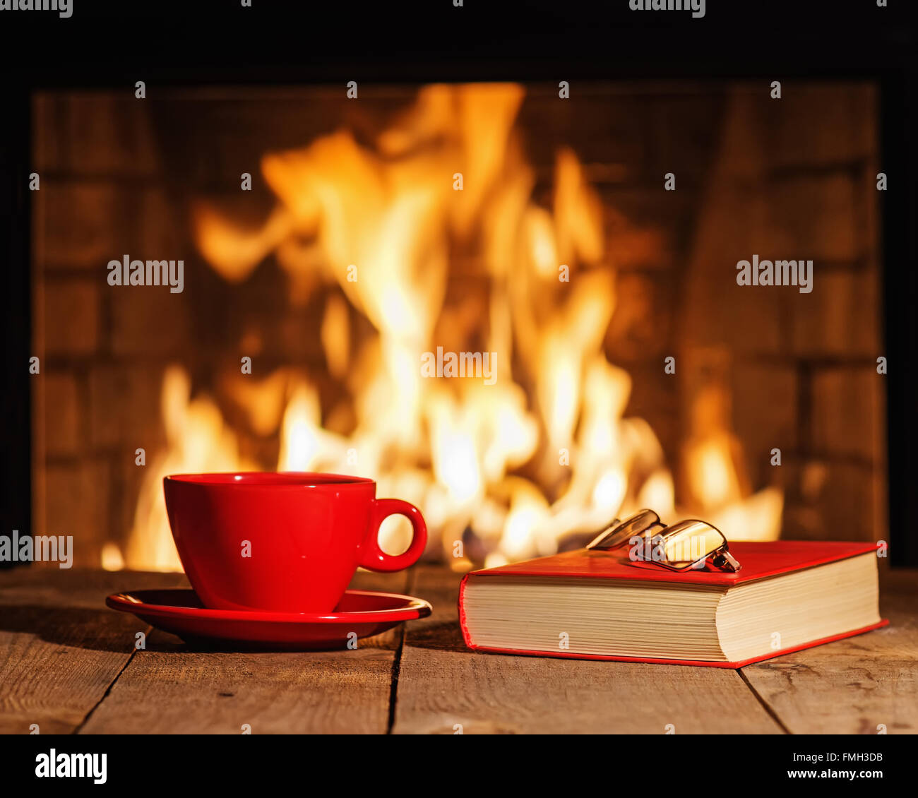 Rote Tasse Tee oder Kaffee, Gläser und altes Buch Kamin auf Holztisch. Winter und Weihnachten Ferienkonzept. Stockfoto