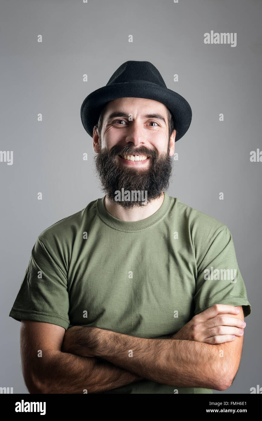 Bärtige Hipster Hut mit Oberlippen piercing freundlich lachend in die Kamera. Kopfschuss-Porträt über graue Studio-Hintergrund Stockfoto