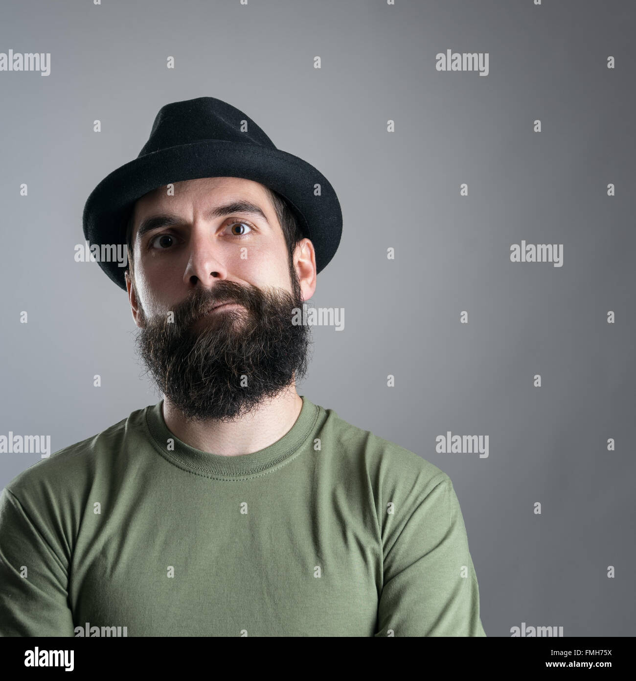 Skeptisch bärtige Hipster in die Kamera starrt. Kopfschuss Nahaufnahme Portrait über graue Studio-Hintergrund mit Vignette. Stockfoto