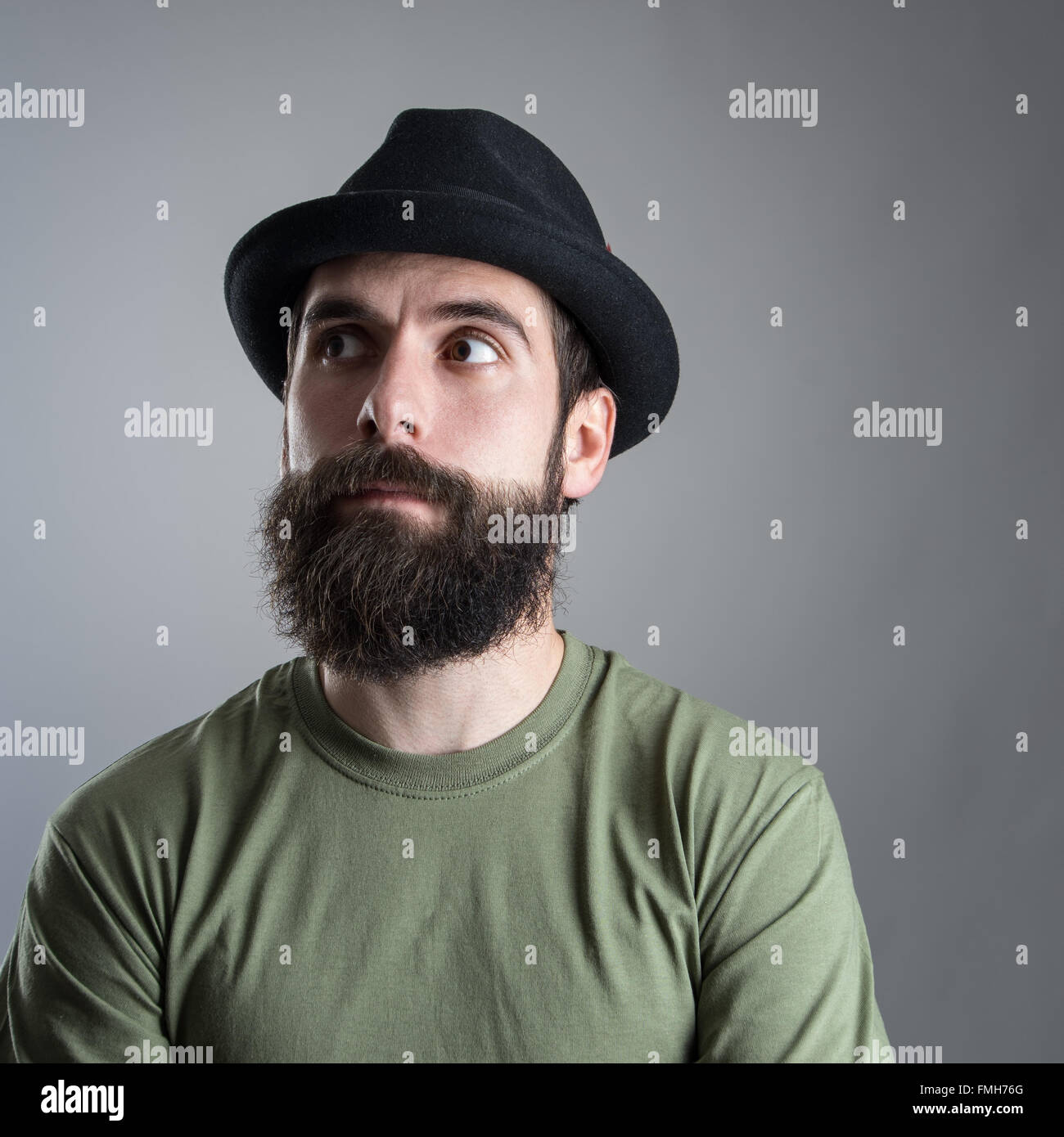 Verwirrt bärtigen Mann mit schwarzen Hut wegsehen. Kopfschuss Nahaufnahme Portrait über graue Studio-Hintergrund mit Vignette. Stockfoto