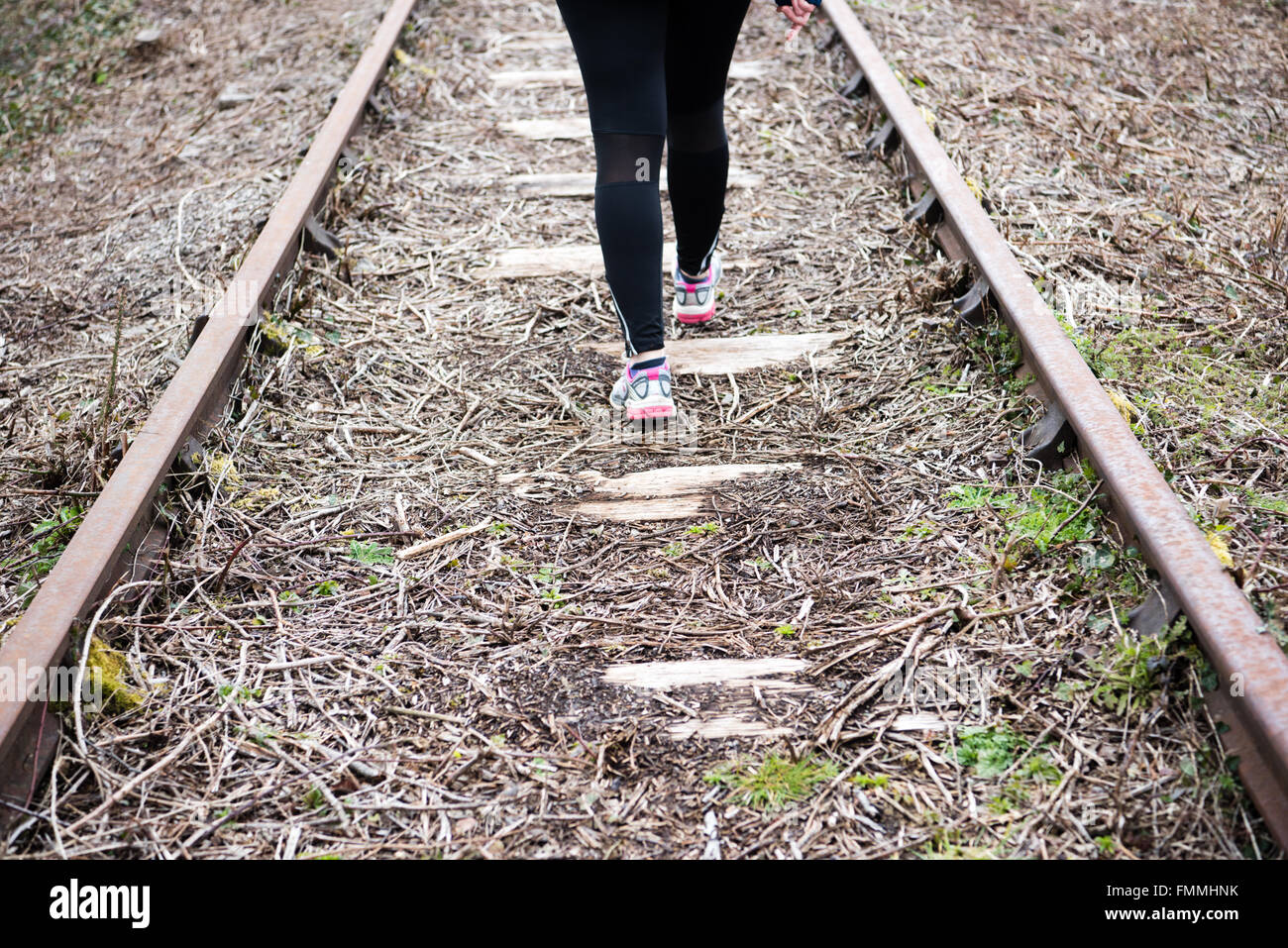 Die Beine der Frau in schwarzen Sport-Leggings und Sportschuhen gehen weg Aus dem Betrachter in der Mitte einer stillgetrachten Schiene Verfolgen Stockfoto